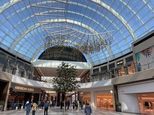 Bright shopping galleries inside Dubai Hills Mall, featuring a large glass ceiling, modern architecture and international retail stores