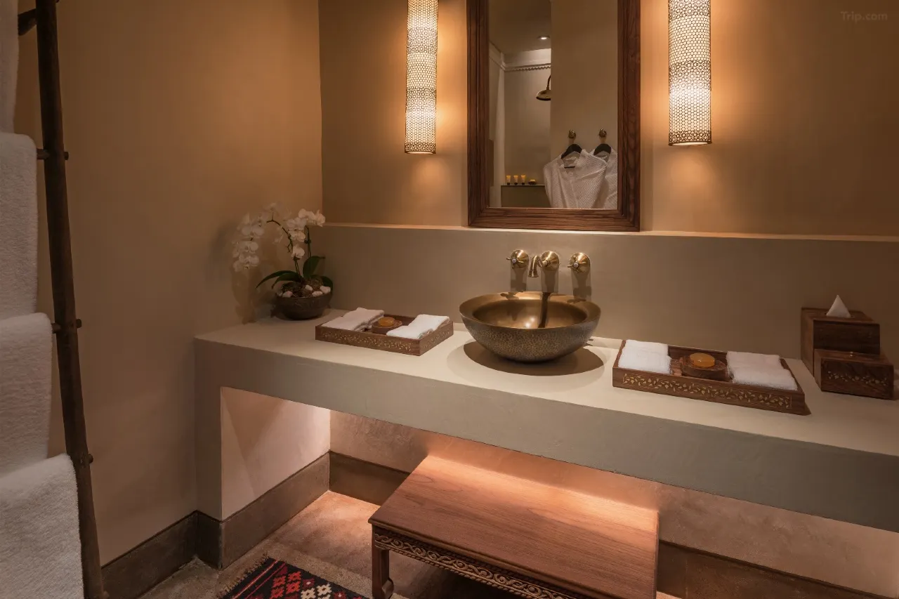 A luxury Arabian-style bathroom vanity featuring a hammered bronze sink, warm ambient lighting from cylindrical wall sconces, and traditional wooden accents with fresh white orchids.