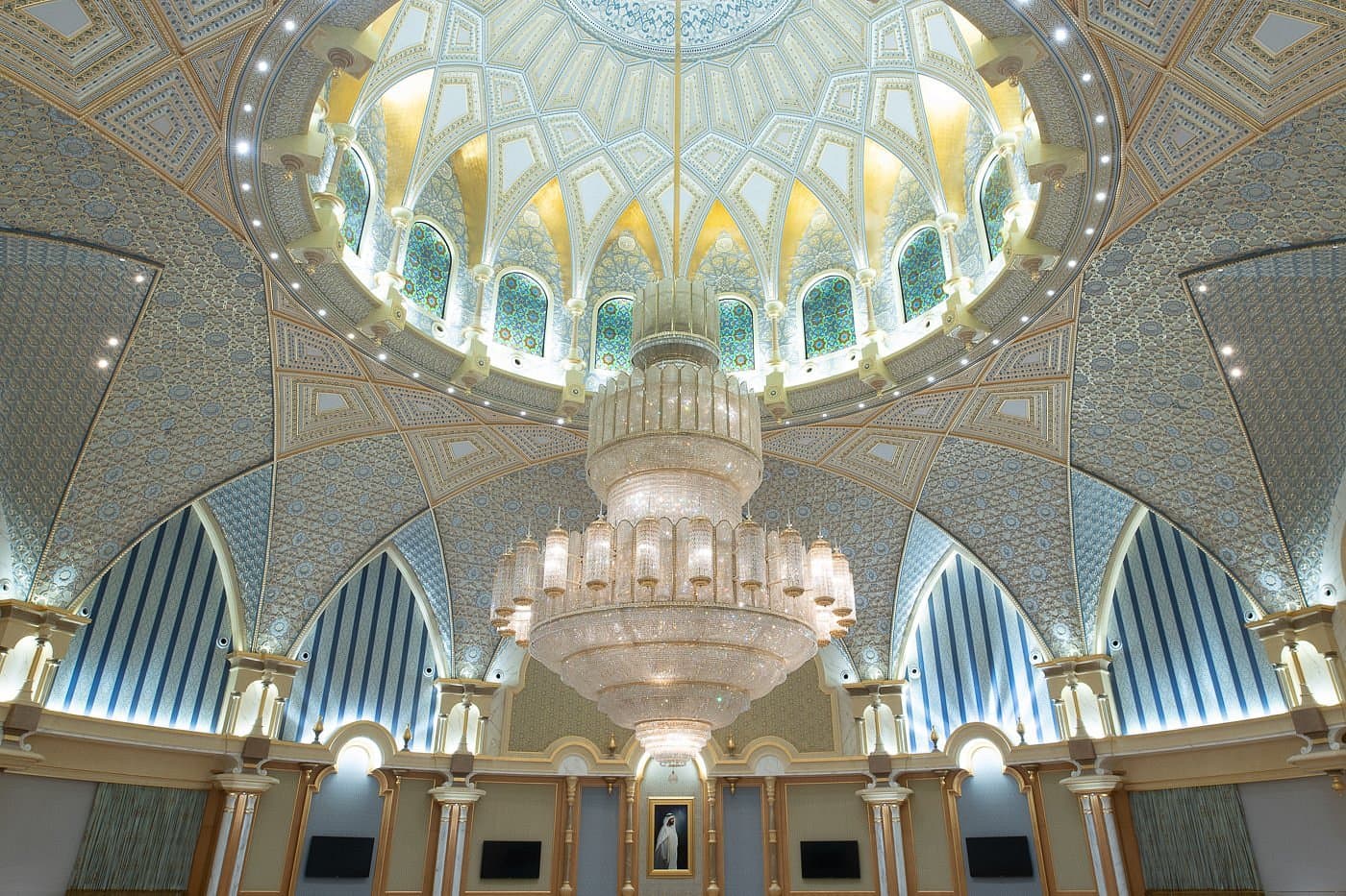 A detailed shot of a palace dome interior, showcasing exquisite Arabian craftsmanship in blue, white, and gold, with a massive crystal chandelier hanging as a centerpiece.