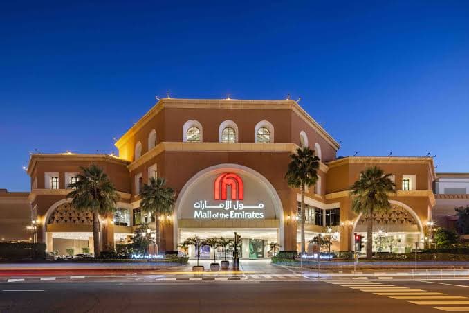 Main entrance of Mall of the Emirates Dubai, featuring elegant architecture and illuminated palm trees at dusk.