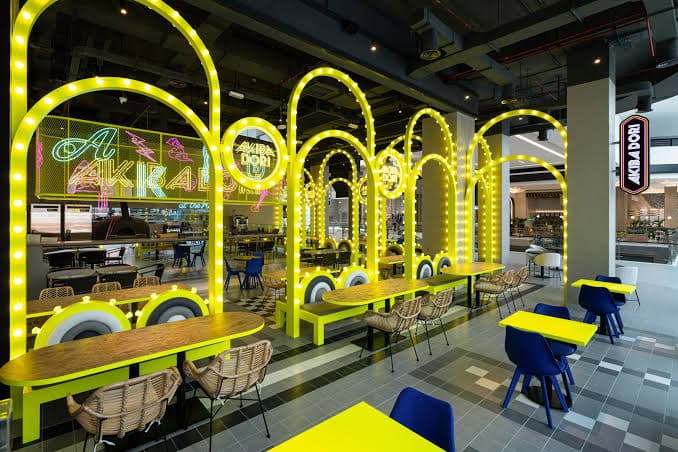 Colorful interior of Akiba Dori restaurant at Dubai Hills Mall, featuring bright yellow neon lights and modern dining areas.