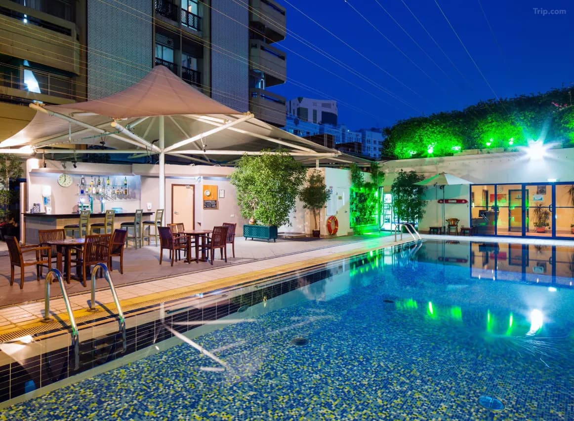 An outdoor swimming pool at night with vibrant blue and green lighting, featuring a poolside bar under a white canopy and patio seating. W 1280 853 R5